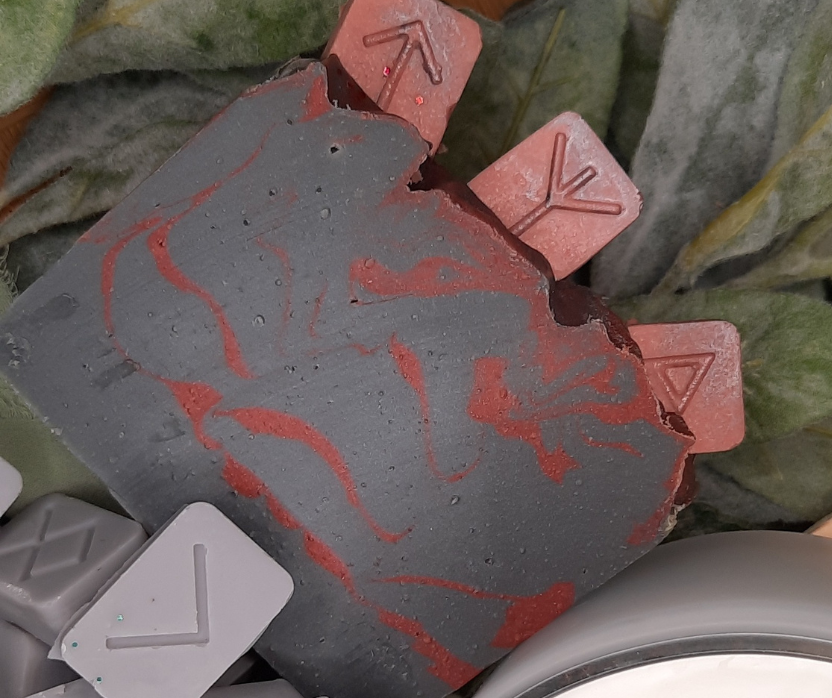 Close-up of a grey soap bar with red designs on a green leafy background